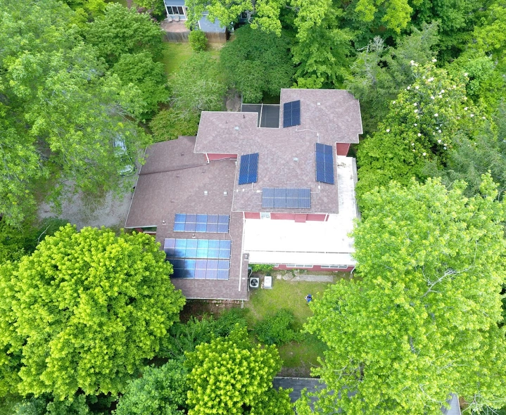 Aerial view of a residential home with rooftop solar panels installed across multiple roof sections and surrounded by mature trees